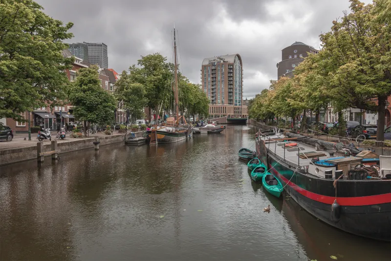 Kanal in Den Haag mit Hausbooten und modernen Gebäuden im Herbst bei bewölktem Himmel
