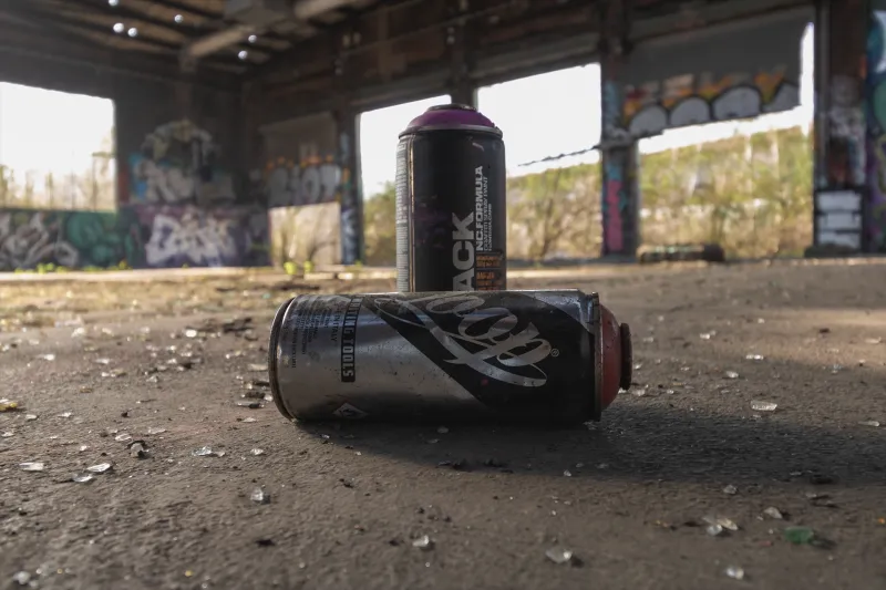 Zwei gebrauchte Graffitispraydosen mit bunten Graffiti bemalten Industriehalle auf dem Boden
